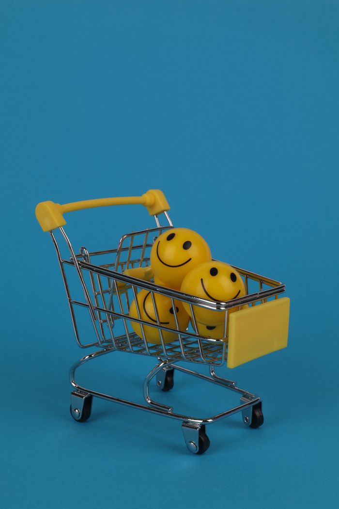 about-04 Shopping cart filled with yellow smiley face stress balls on a vibrant blue background, with ample copy space.