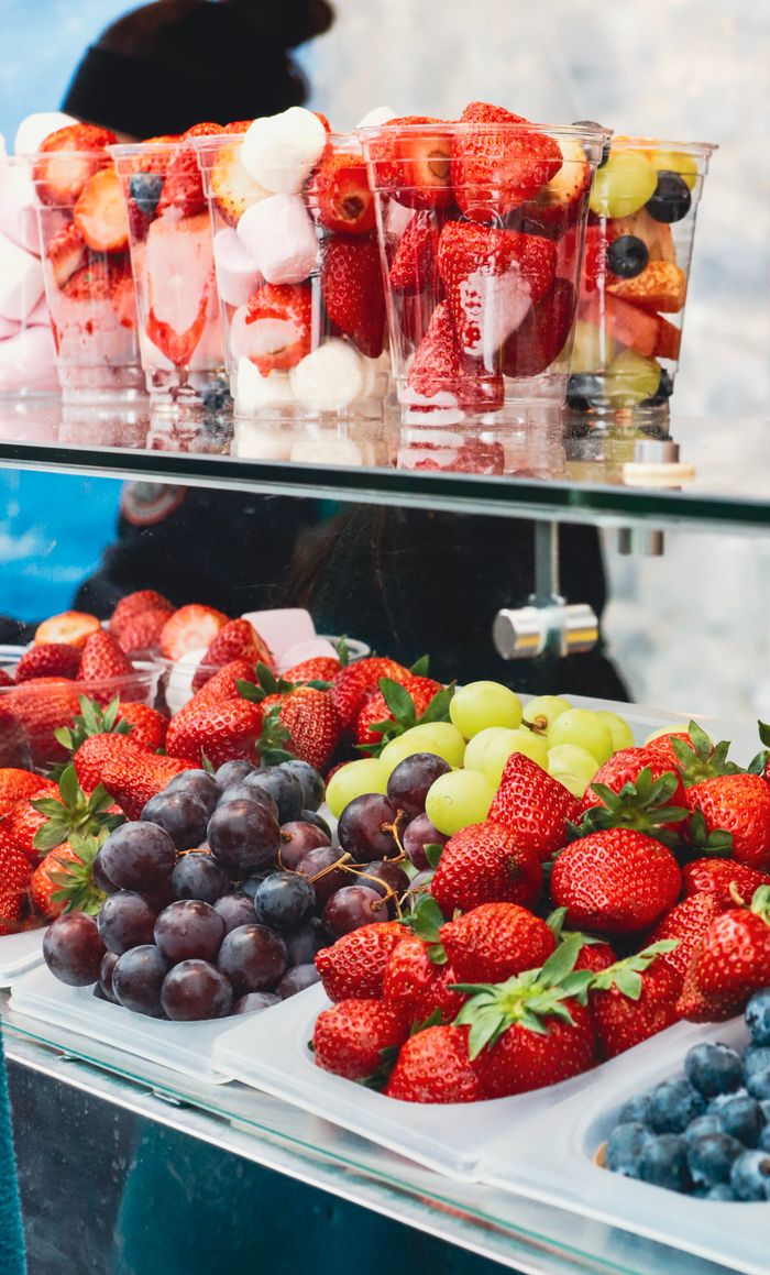 about-07 Vibrant display of fresh strawberries, grapes, and fruit cups in an outdoor setting.